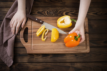 Wall Mural - female hands cutting sweet pepper on wooden table