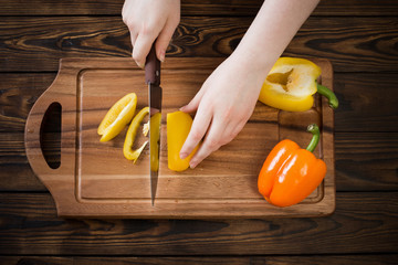 Wall Mural - female hands cutting sweet pepper on wooden table