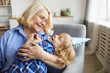 © AnnaStills - Happy grandmother having fun with her grandson and embracing him while they sitting in sofa at home
