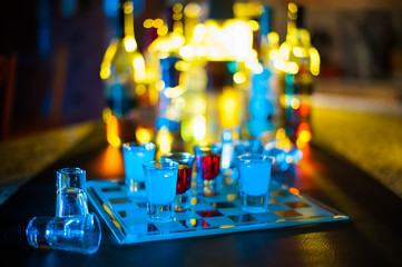 A bar game of shot glass checkers with back lit bottles behind the scene.