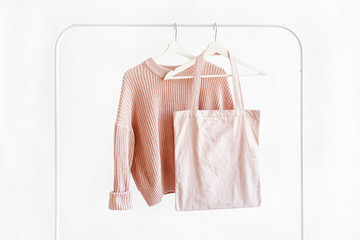 Wall Mural - Feminine pale pink warm sweater with eco bag on hanger on white background. Elegant jumper fashion outfit. Spring wardrobe. Minimal concept.