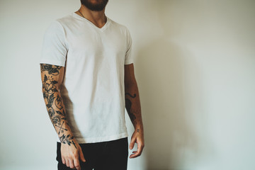 Wall Mural - Cropped photo of a tattooed man dressed in casual clothes demonstrating an empty place for design on a white blank t-shirt. Horizontal mockup.