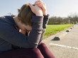 Frustrated woman sitting on parking lot curb holding head in hands