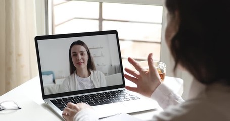 Friends on video chat concept. Over shoulder close up view of young user video calling talking with woman online on computer laptop screen on table. Webcam virtual conference lifestyle communication