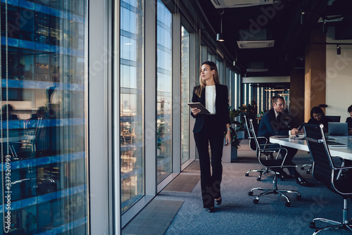 Fotografía Serious female administrative manager in formal suit walking in office with digi