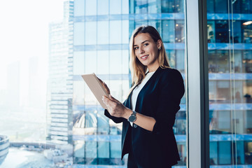 Wall Mural - Half length portrait of cheerful female intelligent manager looking at camera using digital tablet for research in office, smiling business woman in elegant wear banking on touchpad enjoying gadget