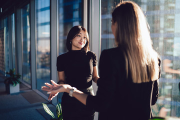 Wall Mural - Young female managers in elegant wear discussing working issues gesturing and feeling confused during conversation, positive formally dressed woman showing don't know emotion talking to employee
