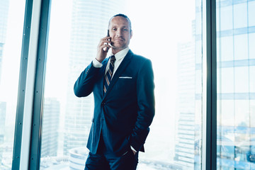 Wall Mural - Half length portrait of handsome caucasian proud ceo in elegant formal wear talking on mobile phone in office interior, smiling 30s confident businessman looking at camera making cellular call