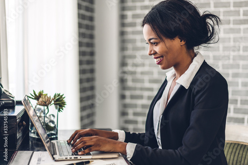 Fotomural Portrait of smiling happy african american black woman relaxing using technology of laptop computer while sitting on table