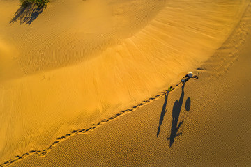 Aerial view of Woman carrying basket at sunset in Bau Trang sand dune, as sun gradually create beautiful setting near paradise beach in Mui Ne, Phan Thiet, Vietnam.