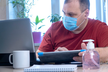 Wall Mural - quarantine due to the coronavirus pandemic. business man working from home, wear a protective mask. Work from home with disinfectant gel. remote work due to the epidemic COVID-19. home office