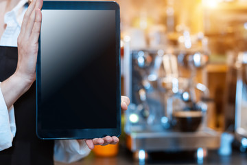 Closeup woman barista, waiter in brown apron uniform is holding tablet computer, ready to take order from client customer in cafe, restaurant. Professional coffee machine on background.