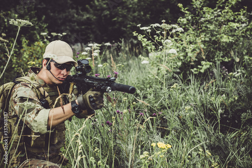 Fotografía A military man or airsoft player in a camouflage suit sits in the grass and aims