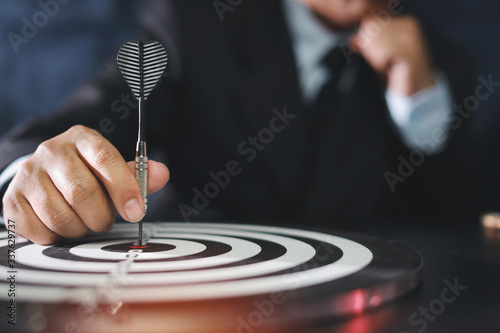 Businessman Hands In Black Suite Sitting And Holding Black Dart Put To Centre Of Target Board On Vintage Table Meaning Of Investment And Achievement Goal Planning And Strategy Concept Stock Photo