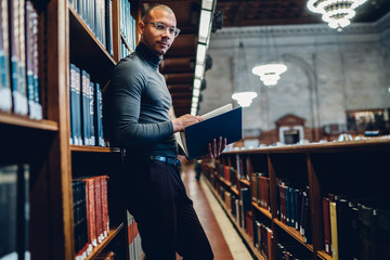 Wall Mural - Half length portrait of intellectual professor of history in bifocal eyewear looking at camera while holding literature book in hand for making research of information for new science publication