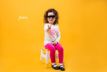 Little girl shows two fingers, gesture of peace on a yellow background