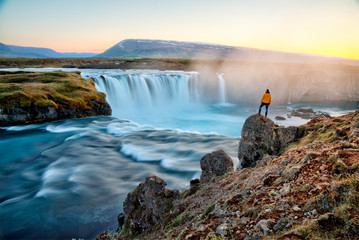 Wall Mural - Man standing by amazing Godafoss waterfall in Iceland during sunset, Europe