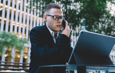 Elegant executive man having phone call while surfing tablet on street