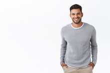 Good-looking Stylish Modern Hispanic Guy With Stylish Haircut, Beard, Wear Grey Sweater Over T-shirt, Hold Hands In Pockets And Smiling Joyfully, Laughing Chatting With Friends, White Background
