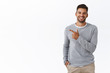Handsome carefree bearded caucasian man in grey sweater, pointing left, discuss product, smiling as talking to you with friendly expression, showing around, introduce promo banner, white background