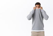 Scared, Timid And Cute Young Guy Feeling Afraid Of Horror Movies, Pulling Sweater On Face And Frowning With Arched Sad Expression, Being Frightened, Standing Shaking Fear White Background
