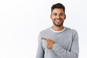 Close-up cheerful good-looking outgoing bearded modern man in grey sweater asking out for coffee, pointing left and smiling, inviting check out see new promo, recommend corporate banner