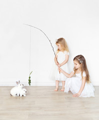 little girls in white dresses feed rabbits grass.