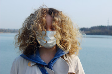 An adorable young teenage girl wearining a mask outdoor, close up shot. Environmental pollution, quarantine, coronavirus, protection concept.Young caucasian girl with curly hair wearing a mask. 