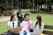 Young asian malay chinese man woman outdoor on park bench study talk discuss point laptop file book