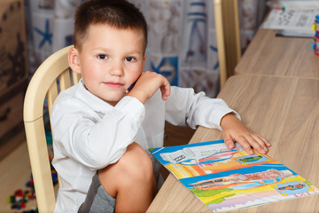 a seven-year-old Caucasian cute boy in a white shirt sits at a Desk at home. . home education