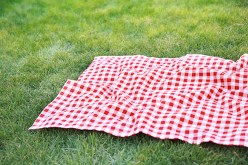 Wall Mural - Red checkered tablecloth on green grass empty copy space,red picnic cloth food advertisement design.