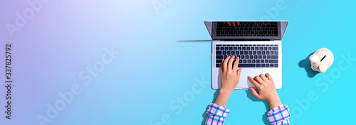 Photographie Person using a laptop computer with a piggy bank - flat lay