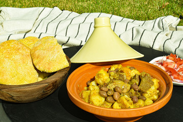 Moroccan Tajine dish with potato olives meat, salad (tamato, onion), and homemade traditional bread on wooden bowl, picnic setup in the nature, cuisine