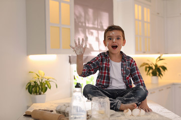 Wall Mural - Emotional little boy with flour on face in kitchen. Cooking dough