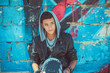 Portrait of a young handsome italian boy with skate and hood posing in the city urban graffiti background looking sidewards