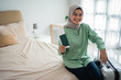 © Odua Images - asian muslim woman smile holding a ticket and suitcase in the bedroom