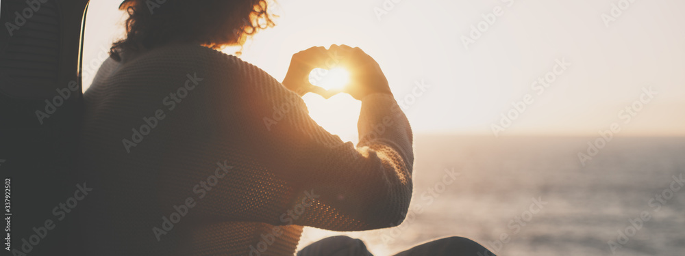 Young traveling female sitting in hat in the trunk of van and enjoing the adventure, woman hipster making heart symbol with hands - obrazy, fototapety, plakaty 