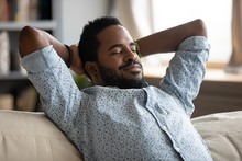Head Shot Tranquil Happy Young African Ethnicity Man Folded Hands Behind Head, Relaxing On Comfy Sofa, Daydreaming Sleeping At Home. Peaceful Carefree Biracial Guy Alone Napping On Couch Indoors.