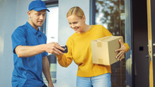 Beautiful Young Woman Meets Delivery Man Who Gives Her Cardboard Box Package, She Signs Electronic Signature POD Device. Courier Delivering Parcel In The Suburban Neighborhood. 