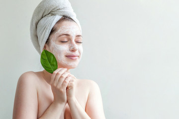 Wall Mural - Minimal beauty portrait woman girl in towel on head applying white nourishing mask or creme on face, green leaf in hand isolated white background. Skincare cleansing eco organic cosmetic spa concept.