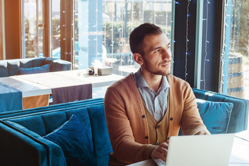 A young man works behind a laptop in a cozy cafe. Business and coworking concept. Portrait of a man.