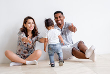 Beautiful Young Caucasian Woman Couple And An African American Man Are Pulling Their Hands To Their Charming Mixed Race Daughter. Concept Of Posing On White Background. Copyspace
