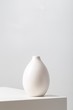 Vertical closeup of a white clay vase on the table under the lights against a white background