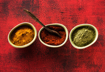 Wall Mural - Indian spices seasoning spicy in bowls on a red background, top view. Ground chili, turmeric curry and cardamom