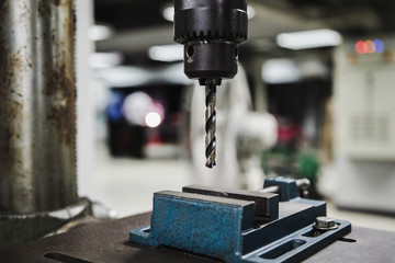 Industrial metal drill head in the workshop room with blurred background of students working on other workshop projects