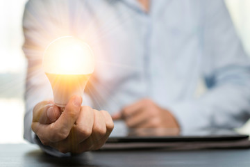 Fototapete - Businessman hands holding the light bulb that is illuminating on the table. Creative protecting patents and ideas concept.