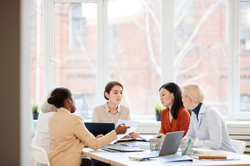 Wide angle view at diverse female business team discussing project while sitting at table during meeting in conference room, copy space