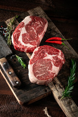 Raw rib eye steak of beef on a wooden Board with a meat cleaver and seasonings