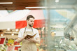 Waist up portrait of bearded man wearing apron and holding notebook while doing inventory count in supermarket, copy space