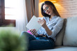 © nenetus - Concentrated young woman using her digital tablet while sitting on sofa at home.